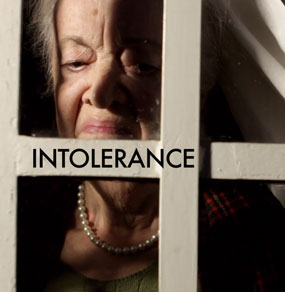 Una donna anziana dietro una finestra con aria disgustata e la scritta Intolerance sopra un infisso bianco
