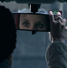 Una donna si specchia nel retrovisore di una macchina e ha una ferita sulla fronte
